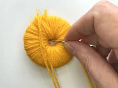 a person is knitting yarn on a white surface with a yellow ball in the foreground