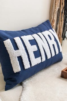 a blue pillow with the word hemba on it sitting on a white couch next to a wooden block