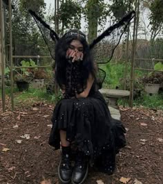 a woman dressed as a fairy sitting on top of a pile of dirt with her hands in her mouth