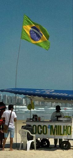 people are standing on the beach near an ice cream cart with a flag flying in the wind