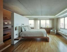 a large bedroom with hardwood floors and white walls, along with windows overlooking the city