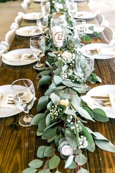 the table is set with white plates and silverware, greenery, and candles