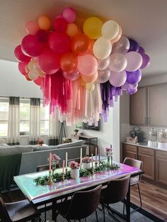 a dining room table with balloons hanging from the ceiling above it and flowers on the table