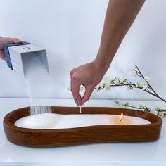 a person is pouring water into a wooden tray with white flowers on it and a candle in the center