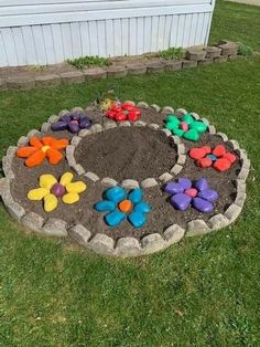 a flower garden made out of rocks in the grass with flowers painted on it and some dirt