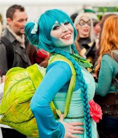 a woman with blue hair and braids standing in front of other people wearing costumes