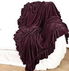 a bed covered in a purple blanket on top of a wooden floor next to a white wall