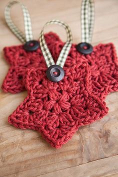 two red crocheted star ornaments with black buttons on them sitting on a wooden surface