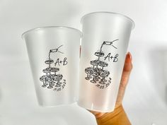 two plastic cups with drawings on them being held up