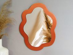 an orange mirror sitting next to a white vase