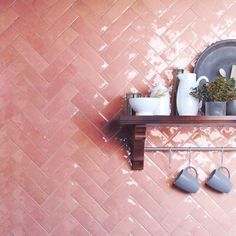 a shelf with coffee cups and mugs on it in front of a pink tiled wall