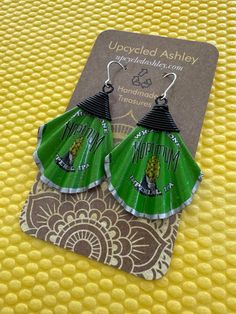 the green fan shaped earrings are sitting on top of a yellow tablecloth with an ornate pattern