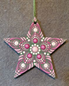 a pink and green star ornament hanging on a gray carpeted floor with white dots