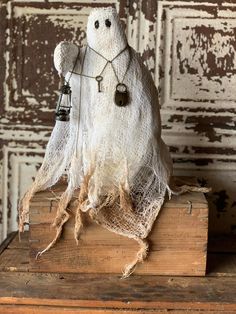 a white cloth ghost sitting on top of a wooden box with two bells hanging from it's neck