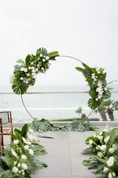 an outdoor ceremony setup with greenery and white flowers on the aisle, overlooking the ocean