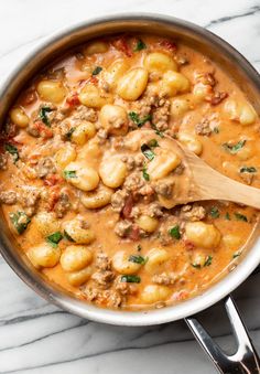 a pot filled with pasta and meat in tomato sauce on top of a marble counter