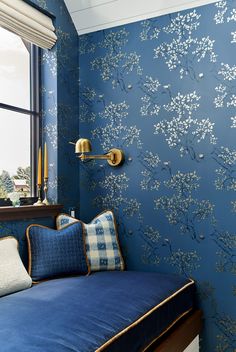 a room with blue walls and white flowers on the wall next to a bed in front of a window