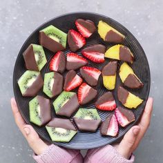 a person holding a plate with sliced fruit and chocolates on it in front of their hands