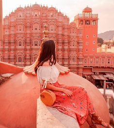 a woman sitting on top of a large pink building with a clock tower in the background