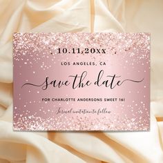 save the date card with pink and gold glitters on white satin fabric, in front of an elegant background