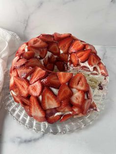 a cake covered in sliced strawberries on top of a glass plate next to a napkin