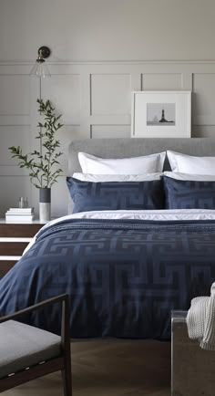 a bed with blue and white comforter in a bedroom next to a potted plant