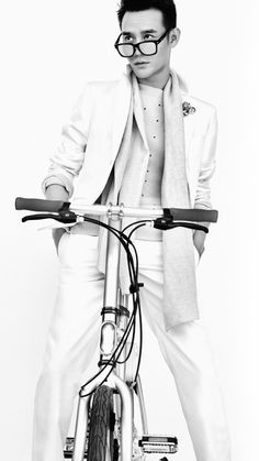 black and white photograph of a man on a bicycle wearing glasses, with one hand on the handlebars