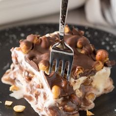 a fork is stuck into a piece of dessert on a plate with nuts and chocolate