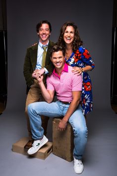 two men and a woman sitting on top of a wooden block posing for the camera