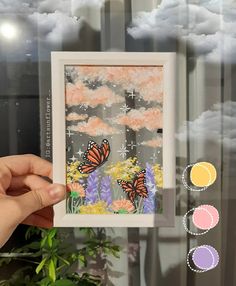 a hand holding up a framed photo with some flowers and clouds in the back ground