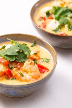 two bowls filled with soup and garnished with cilantro, red peppers, and parsley