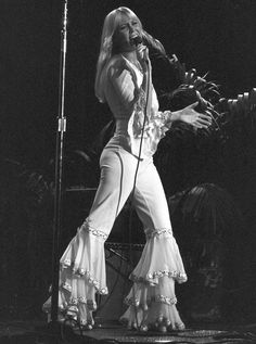 a woman in white outfit standing on stage holding a microphone and singing into a microphone