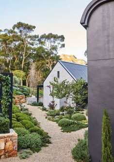 an outdoor garden is shown with various plants and trees in the foreground, along with a stone path leading to a white building