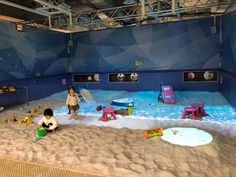 two children playing in an indoor play area with sand and plastic toys on the floor