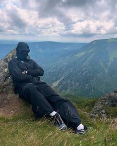 a man sitting on top of a mountain next to a lush green forest covered hillside