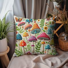 a pillow with colorful mushrooms on it sitting next to a potted plant and window