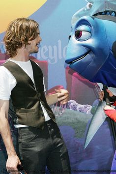 a man standing next to a giant blue fish balloon on top of a red carpet