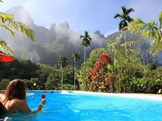 a woman sitting in a pool holding a wine glass and looking out at the mountains