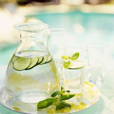 a pitcher of water with cucumber slices and mint on the rim next to glasses