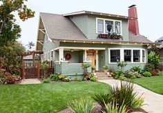 a green house with lots of plants in the front yard and landscaping on both sides