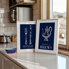 two framed pictures sitting on top of a counter next to a blue bowl and fork