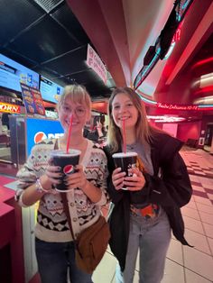 two young women standing next to each other holding drinks in their hands and smiling at the camera