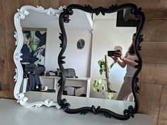 a woman taking a selfie in front of a large black and white framed mirror