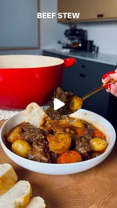 a woman is spooning stew into a bowl with bread on the table next to it