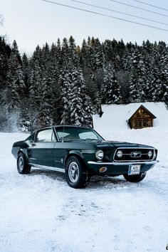 an old mustang sitting in the snow next to a cabin