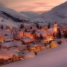 a snowy town with mountains in the background at night, lit up by street lights