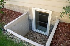 an open window in the side of a house with grass growing around it and rocks on the ground