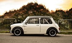 an old white mini car parked on the side of the road in front of some trees