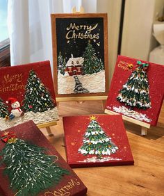 four christmas cards are sitting on top of a wooden table, decorated with snow and trees