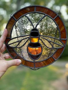 a hand holding up a stained glass window with a bee on it's side